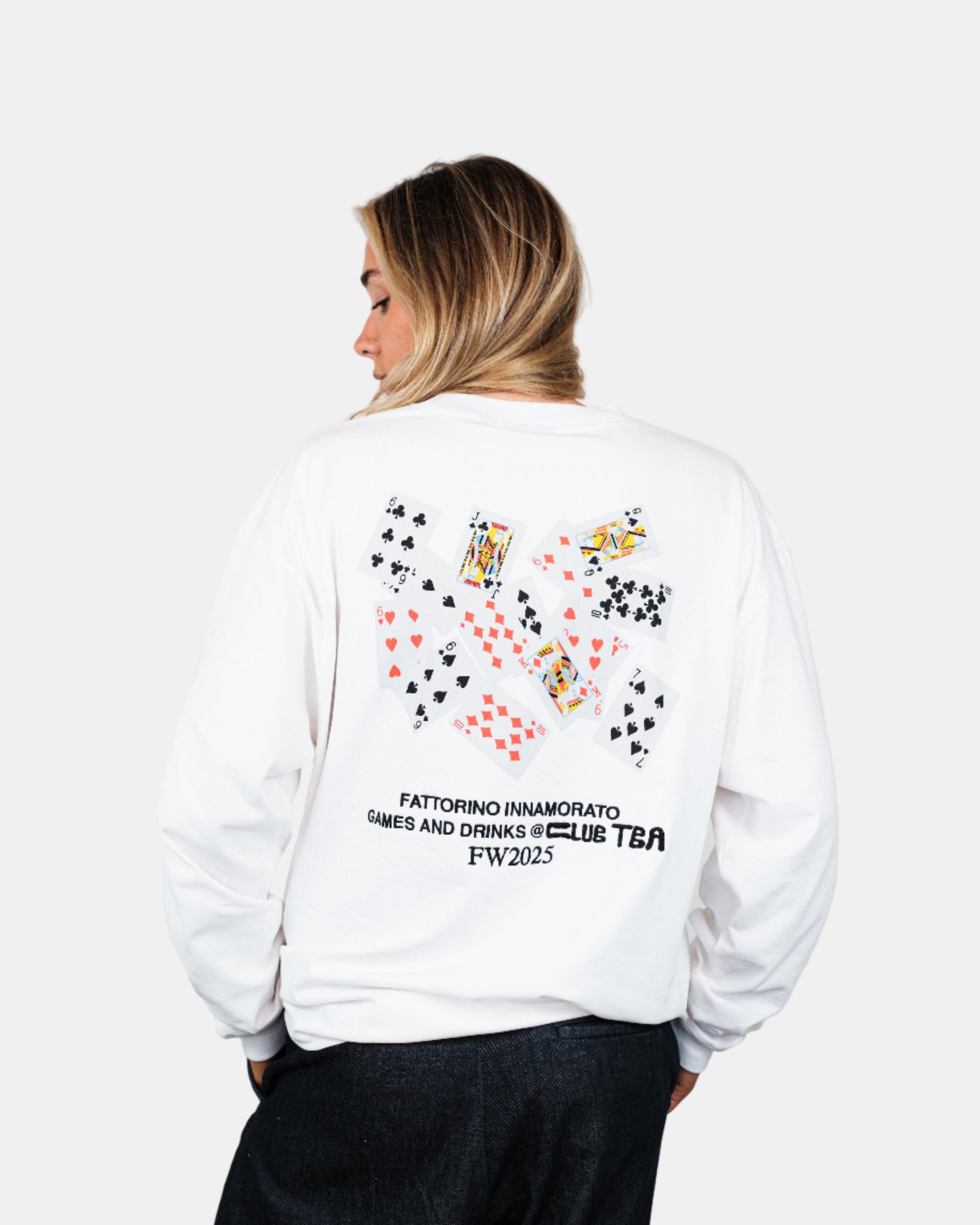 woman wearing a white longsleeve tshirt with colorful graphics and text on the back, standing against a plain background. Fattorino Innamorato play cards 