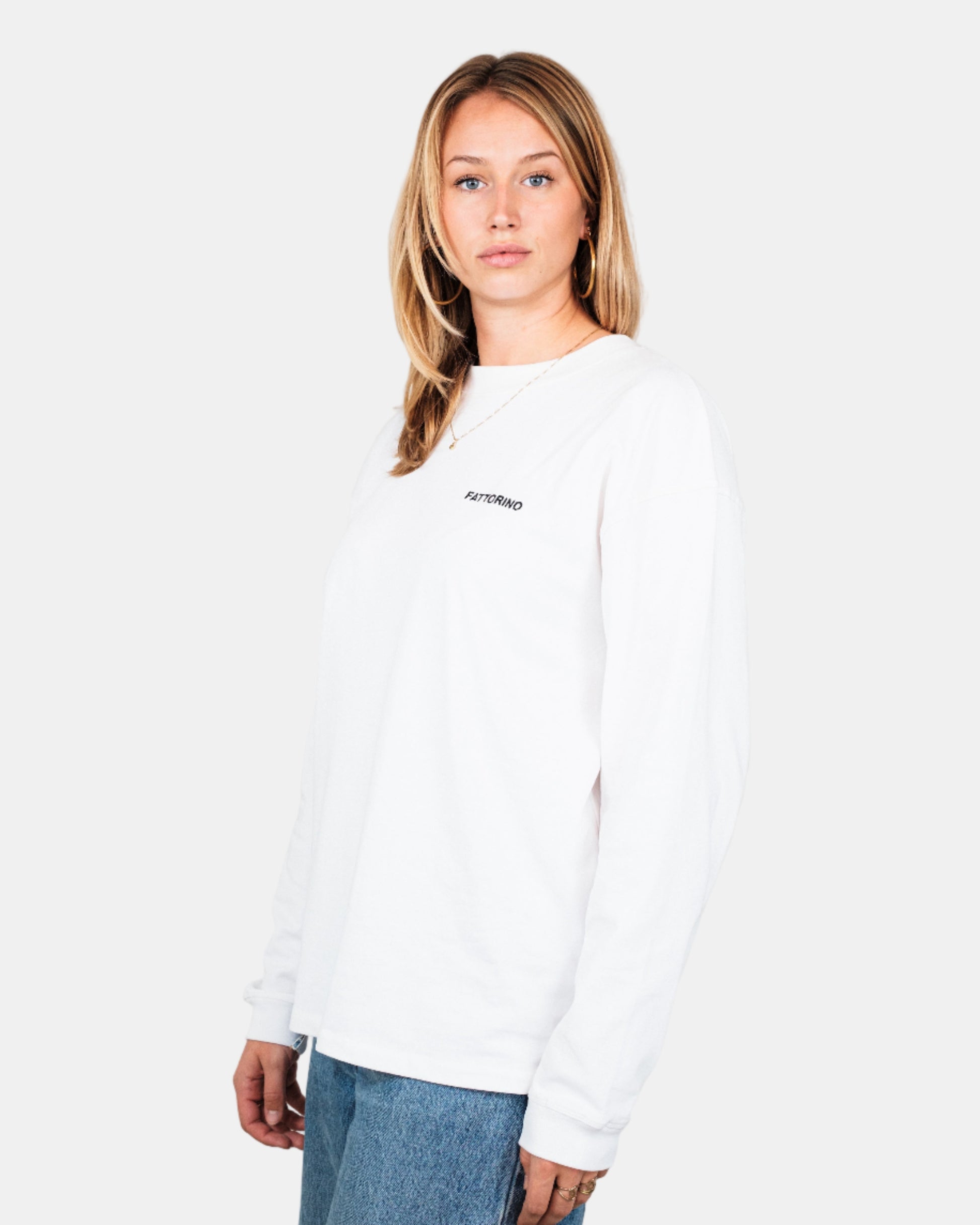 Person wearing a white long-sleeve shirt with a logo on a plain background. Fattorino Innamorato Dutch
