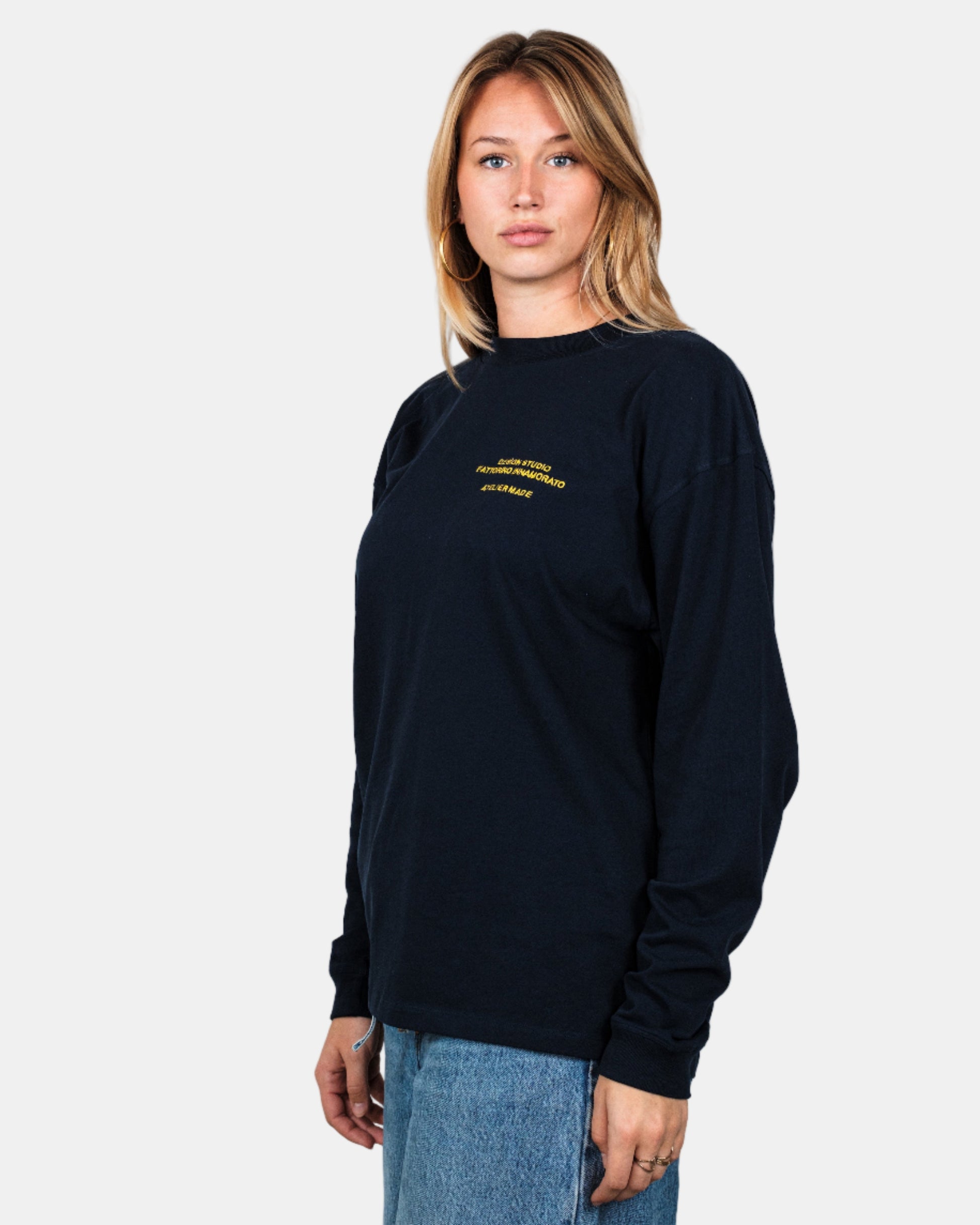 Person wearing a navy longsleeve shirt with yellow text and graphics on the front, standing against a white background. Fattorino Innamorato maison navy longsleeve