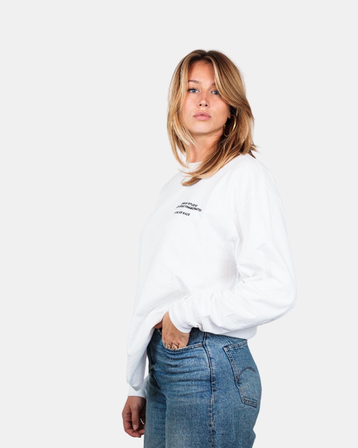Person wearing a white longsleeve tshirt with a logo and blue jeans on a plain background. Fattorino Innamorato pool longsleeve