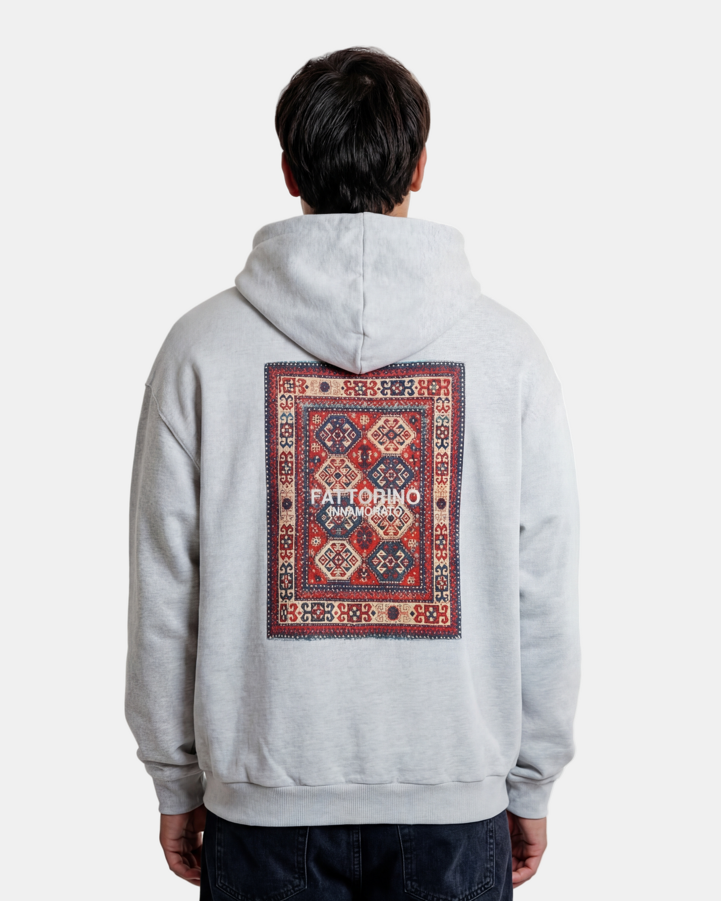 Person wearing a light gray hoodie with a patterned rug design on the back against a white background. Fattorino Indian rug grey hoodie