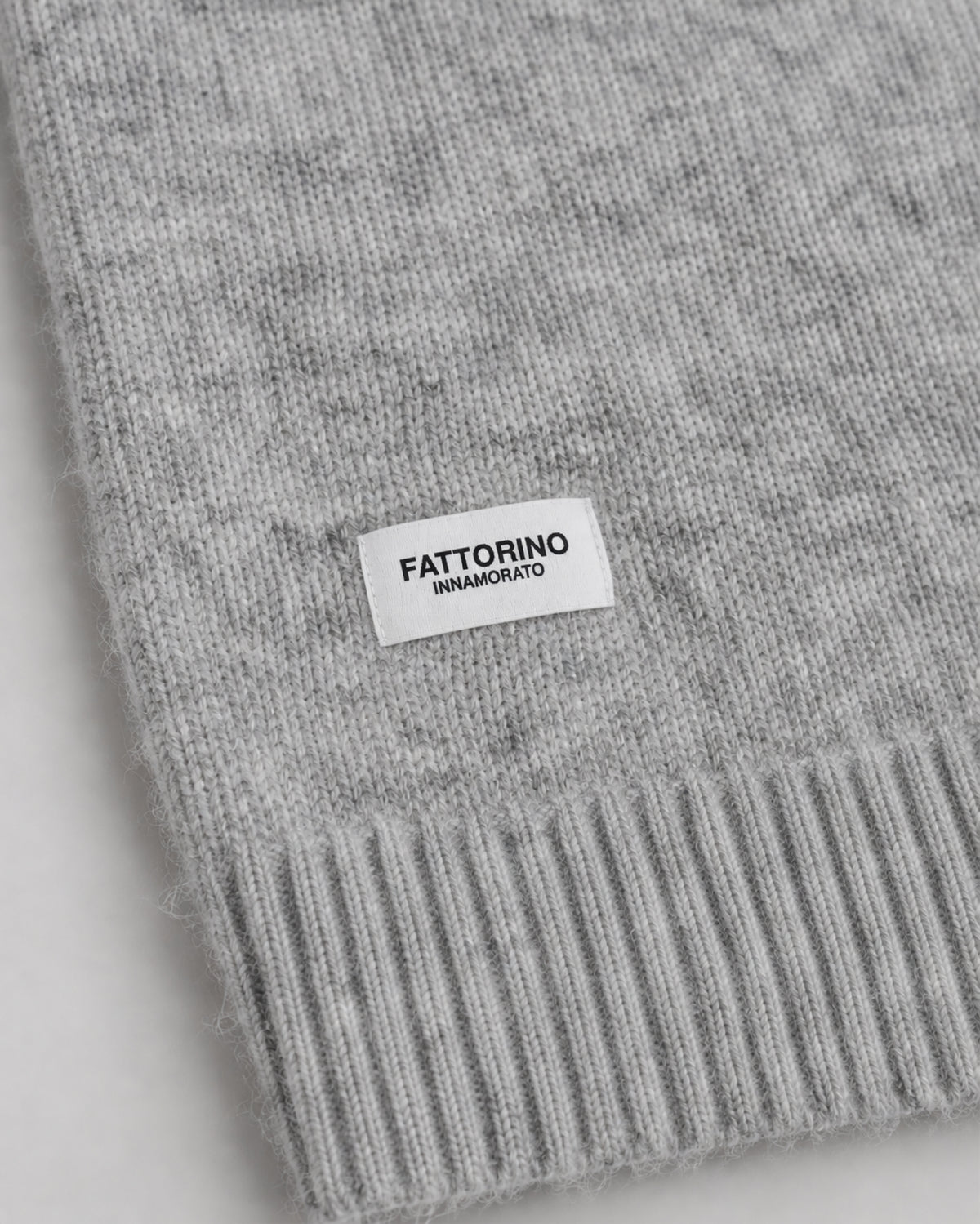 Close-up of a light gray knit sweater with a ribbed cuff and a small white label reading FATTORINO INNAMORATO.
