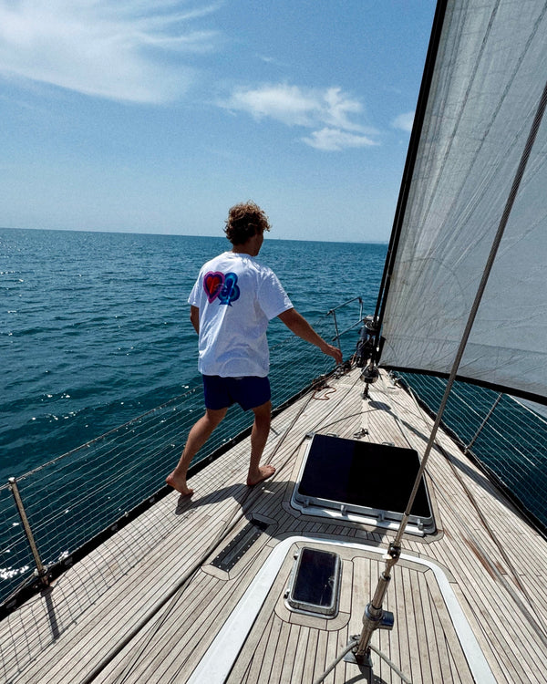 Person on a sailboat looking out at the ocean with a clear blue sky. Fattorino Innamorato white play tshirt