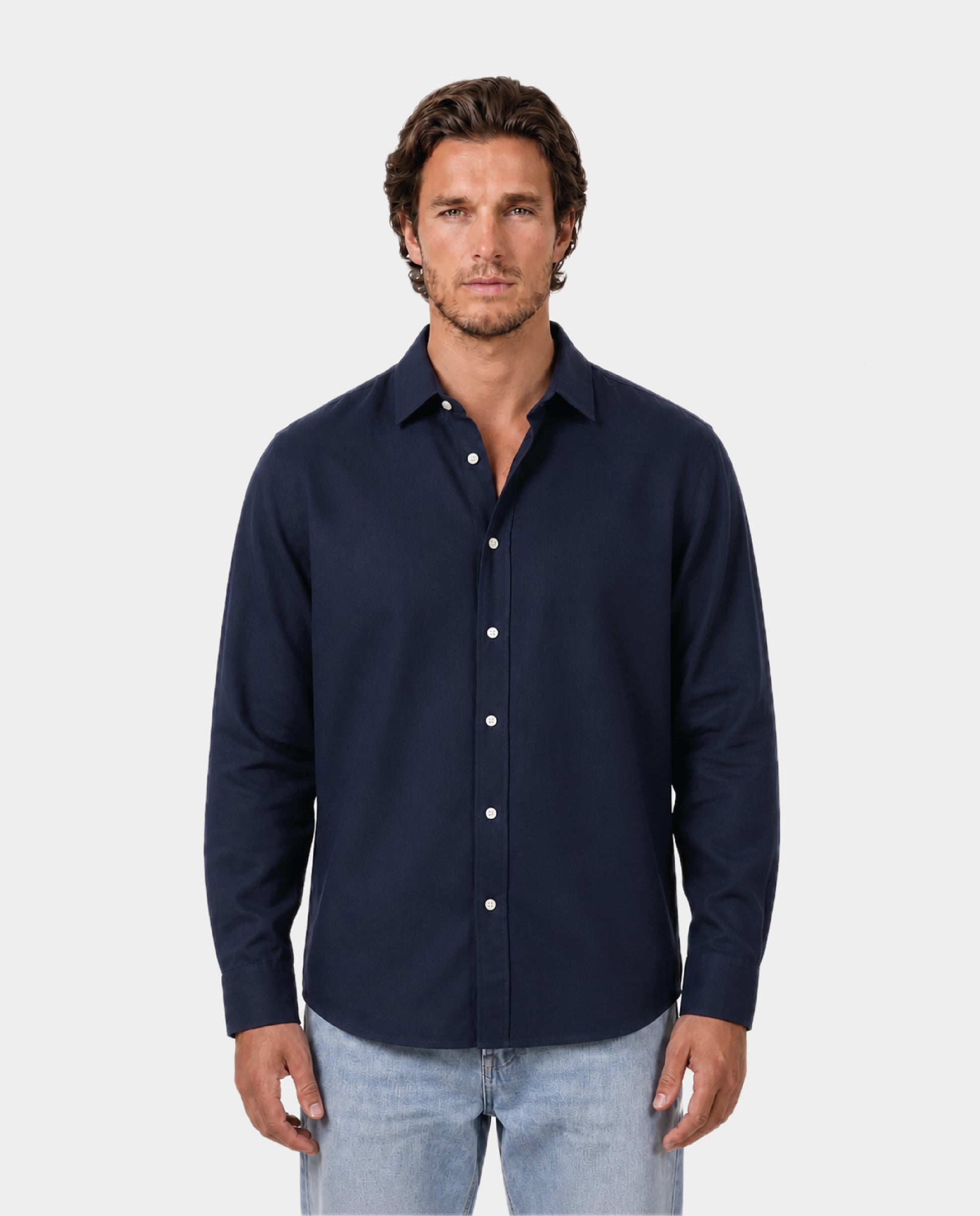Man wearing a navy button-up shirt and light blue jeans on a white background. Fattorin Innamorato navy cotton shirt. Oxford shirt 